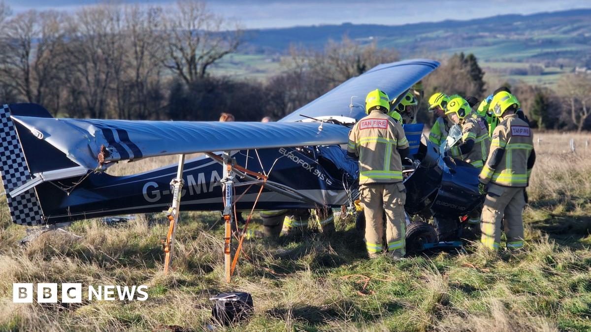 Plane wreckage in a field. Firefighters stand on the right of the craft