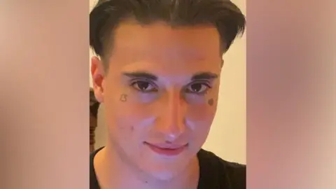 Met Police Image of Aidan Chapman looking at the camera, a man with dark floppy hair and a tattoo under each eye - one of a broken heart and the other the number 13