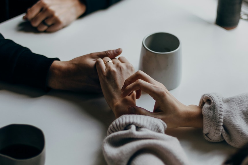 Clasped hands on a table with a cup of coffee nearby