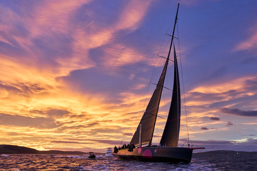 Yacht and two smaller craft on a river with sunrise sky.