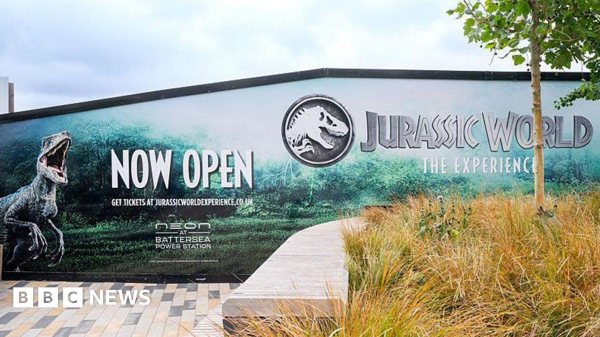 The exterior of the exhibition. There are billboards advertising the Jurassic World experience with pictures of dinosaurs.