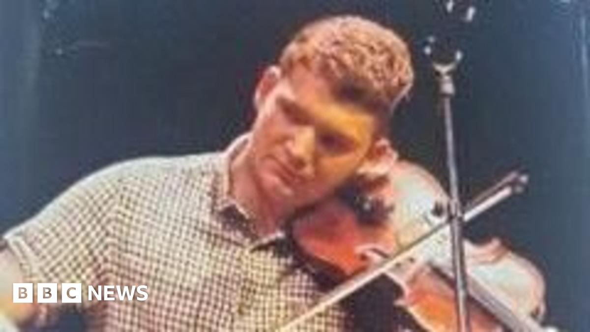 A man in a checked shirt plays the fiddle