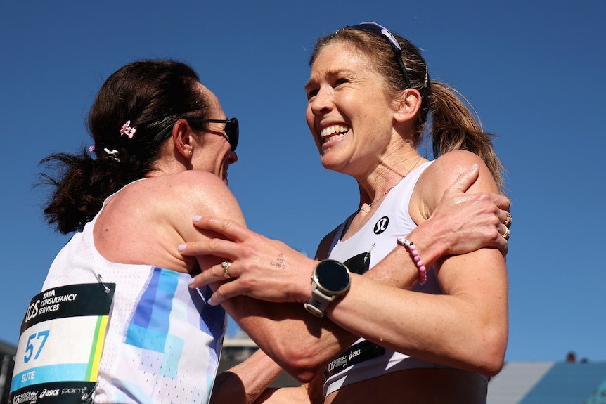 Two female athletes hold each other by the arms in celebration