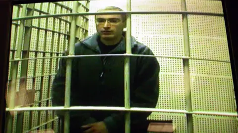 AFP Russia's richest man and oil magnate Mikhail Khodorkovsky is seen in his cage in "Matroska tishina" prison on a TV screen during a video-link in the courthouse in Moscow, 15 January 2003
