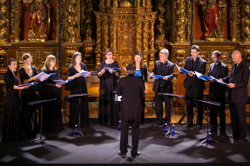 10 singers from the Tallis Scholars sing in the round in front of an ornate gold altar. Peter Phillips conducts in front.