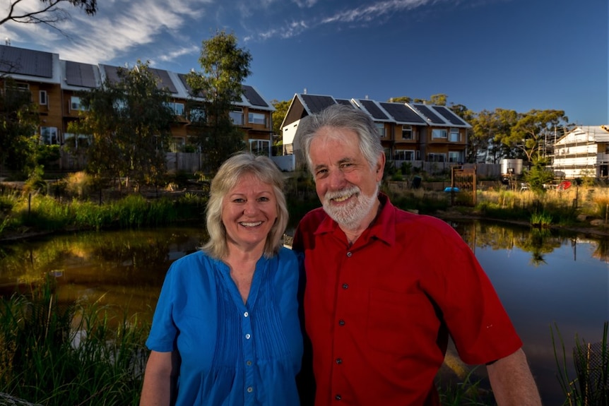 A couple smile together. She wears a blue shirt and he wears a red shirt.