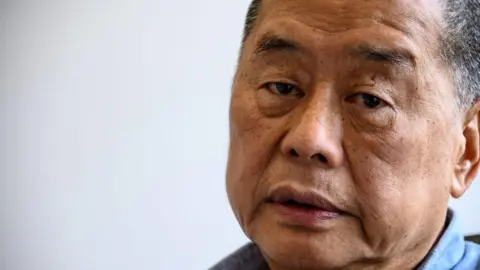 AFP via Getty Images Extreme close up of Jimmy Lai wearing a blue collared shirt looking into the camera