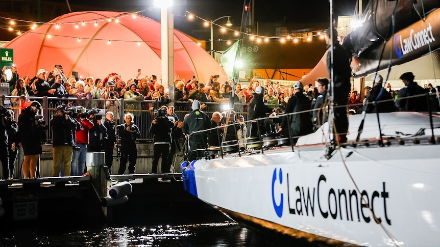 A crowd cheers a crew on a yacht.