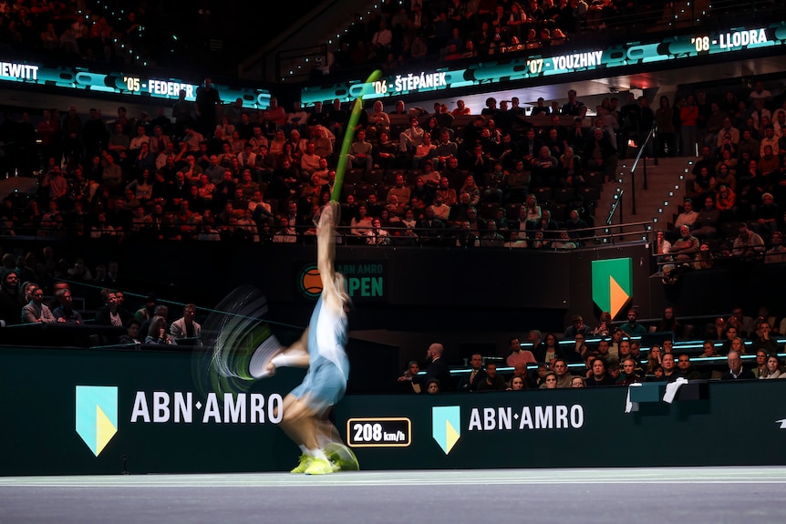 A slow shutter speed image of Carlos Alcaraz serving in a tennis match.