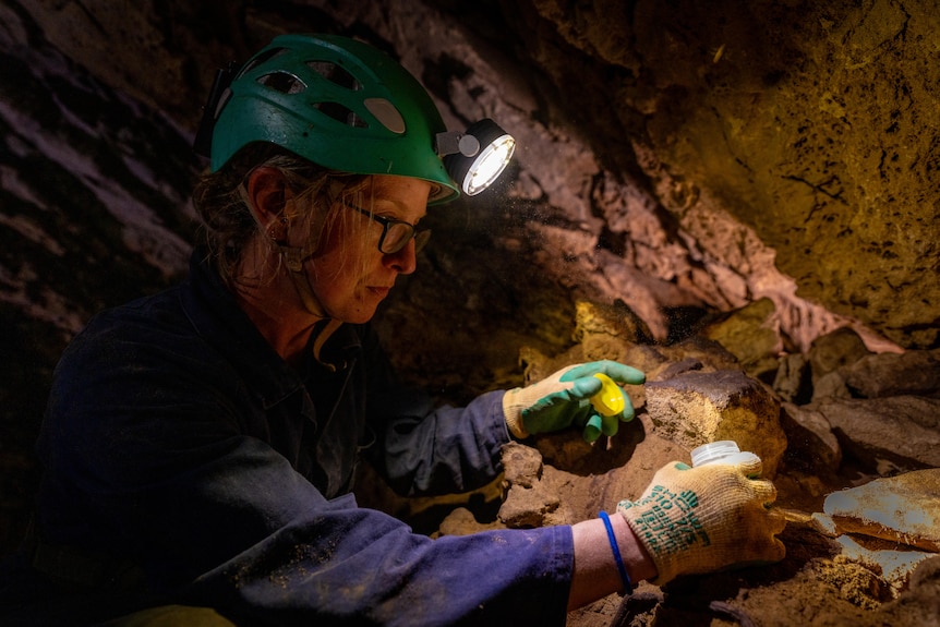 A woman wearing a light helmet inside a cave takes samples