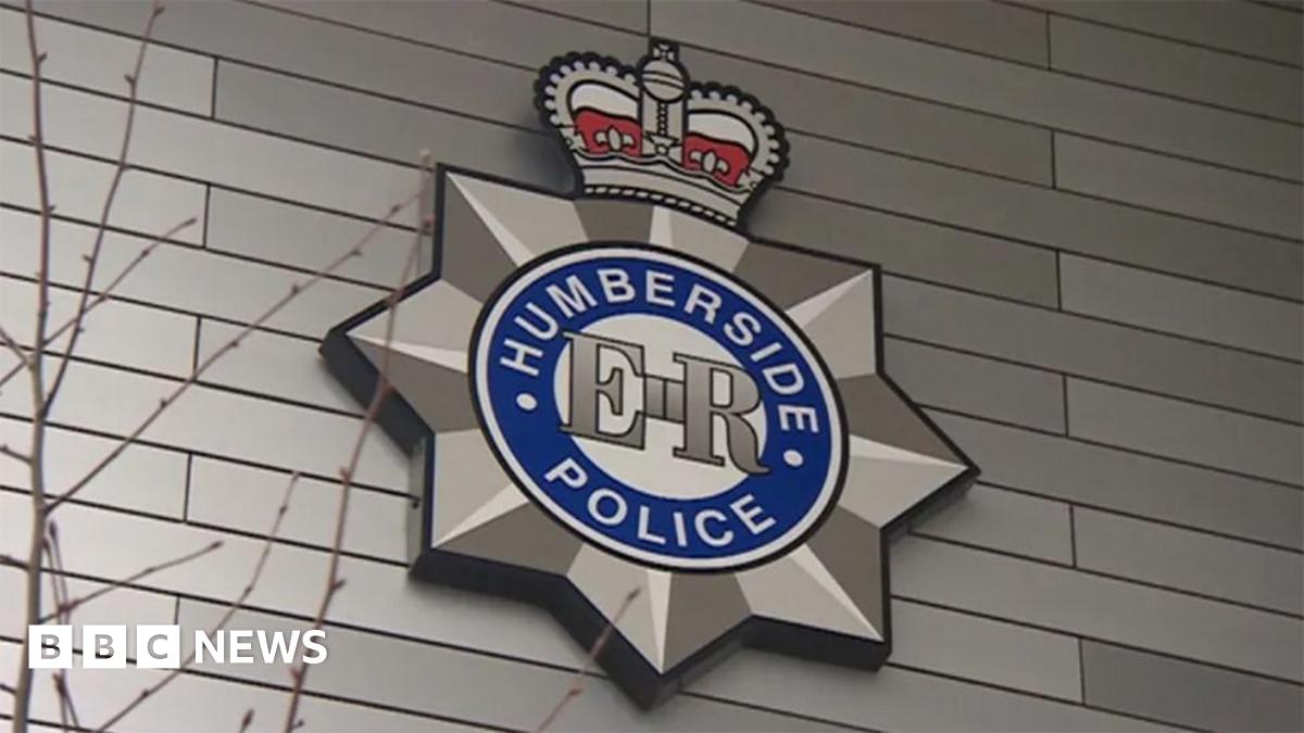 The Humberside Police badge on the wall of a police station. It has the words "Humberside Police" in white letters in a circle with a blue background and the initials "ER" in the middle. A crown sits on top of the badge.
