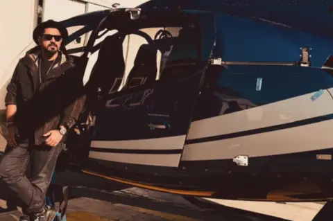Saurabh Luthra/Instagram Saurabh Luthra stands next to a helicopter wearing a black jacket and black jeans. 