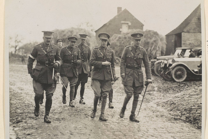 Men in uniform walk through a town looking solumn