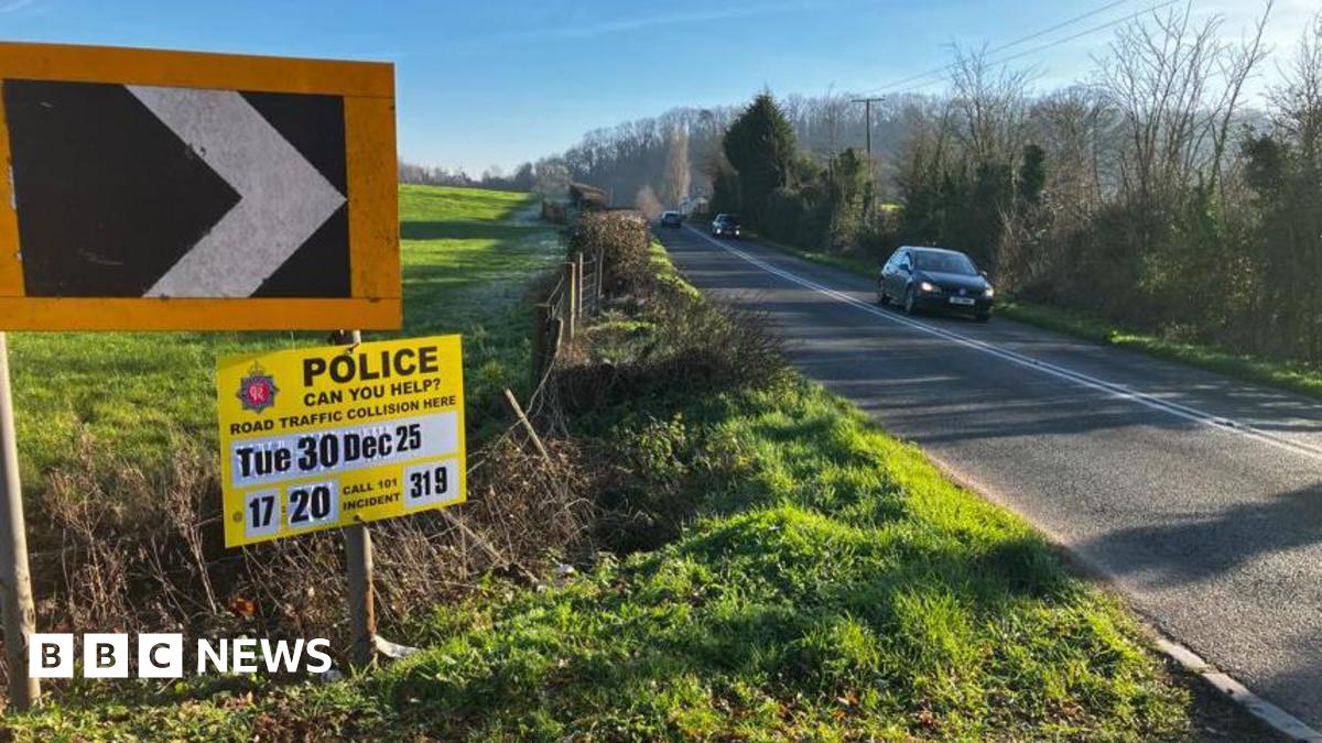 A country lane on a sunny winter day. There is a field on the left hand side and a line of trees on the right. There is a yellow police sign appealing for information about a road traffic collision at 17:20 on Tuesday 30 December 25.