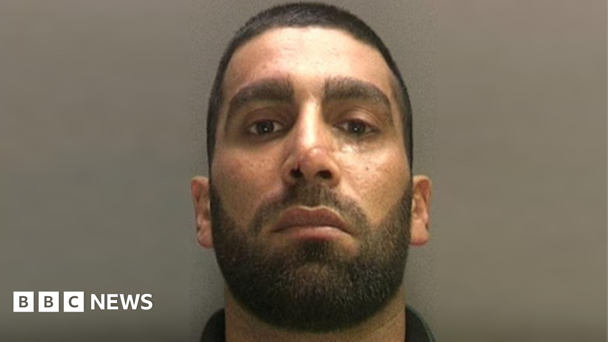 Mugshot of a man with a black beard and hair with a scar on his nose