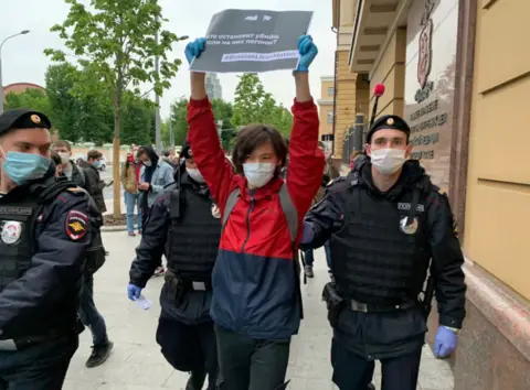Murat Mukashev A young man holds a placard saying "stop the killers if they wear shoulder straps" as police escort him towards the camera