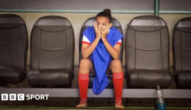 A woman footballer sitting on the bench puts her hands on her face