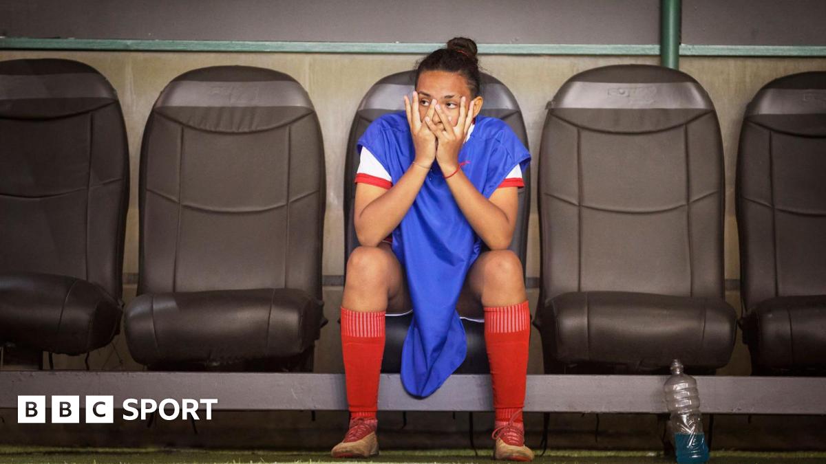 A woman footballer sitting on the bench puts her hands on her face