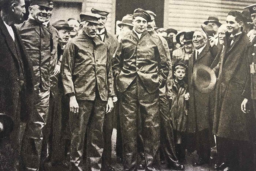 the PM and prince stand in a crowd wearing overalls and caps