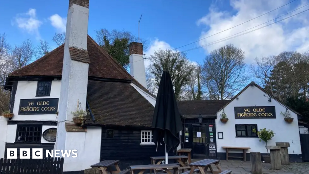 The main structure of Ye Olde Fighting Cocks has an octagonal appearance, attributable to its earliest use as a pigeon house. It has some white external walls with dark brown roof tiles and some black wooden cladding. There are benches and and umbrella outside for customers.