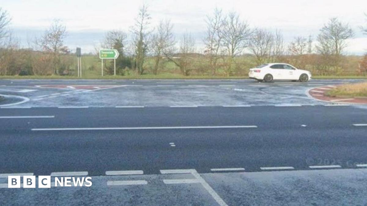 A street view of the road junction where the crash happened at Ingleby Arncliffe. There is a give way line, beyond which are two lanes, then a central turning area and two lanes beyond with trees and fields in the distance.