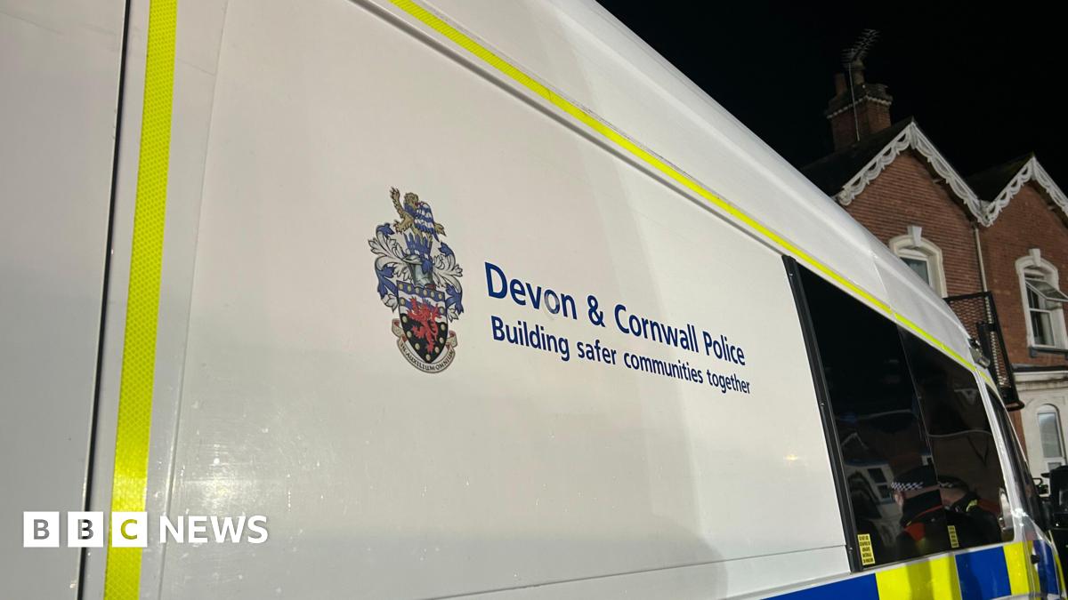 The side of a Devon and Cornwall Police vehicle. The van is white and has a yellow border.