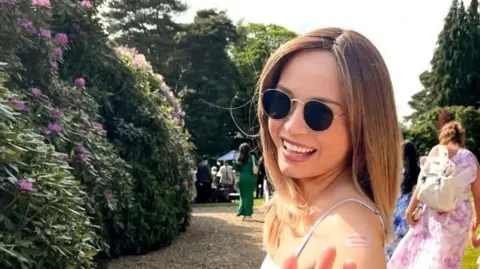 Family handout A woman in a garden wearing sunglasses, she is smiling at the camera.