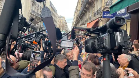 A scrum of photographers surround Nicolas Sarkozy outside a bookshop in Paris, ahead of his book signing