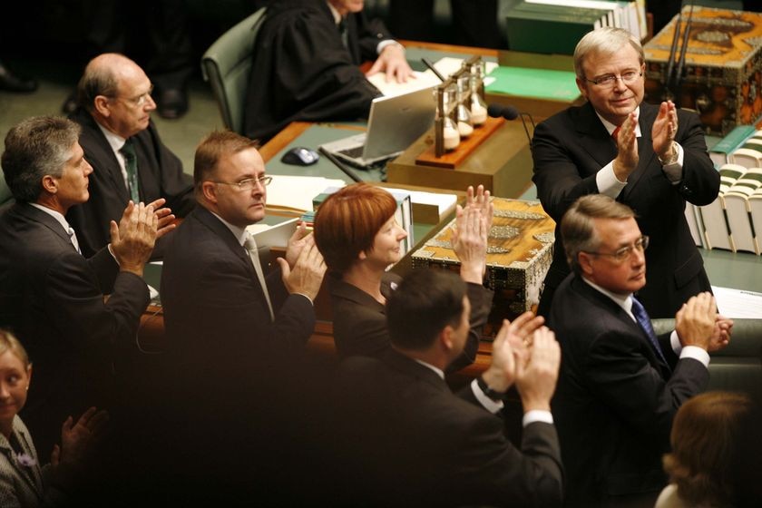 Politicians in dark formal wear, including Julia Gillard, Wayne Swan and Kevin Rudd, applaud while standing the lower house.