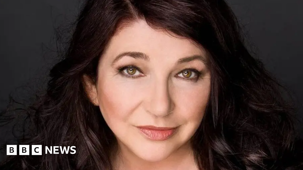 Kate Bush smiling at the camera. She has dark brown hair and eyes.