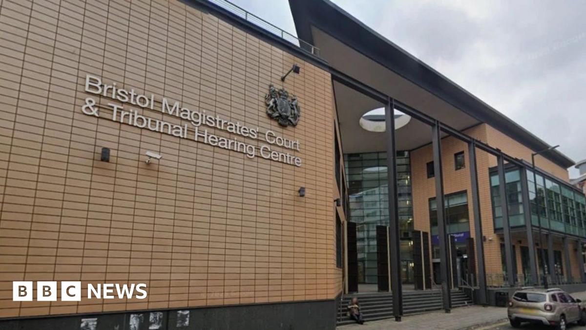 The exterior of the court, which is a large, modern building with a glass entryway and orange/brown brick-like cladding. The sign says 'Bristol Magistrates' Court & Tribunal Hearing Centre' on it.