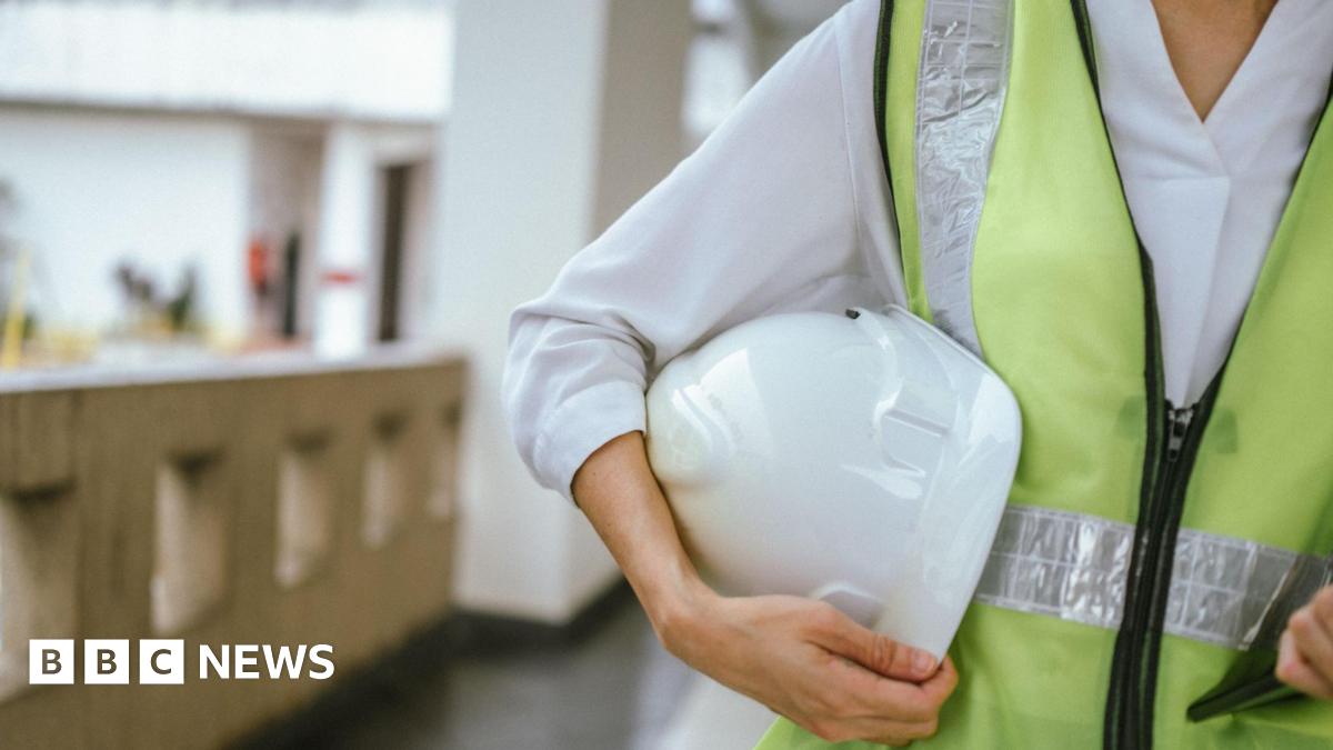 Close-up of a female building inspector standing on-site at a residential building, wearing a safety vest and a white helmet.