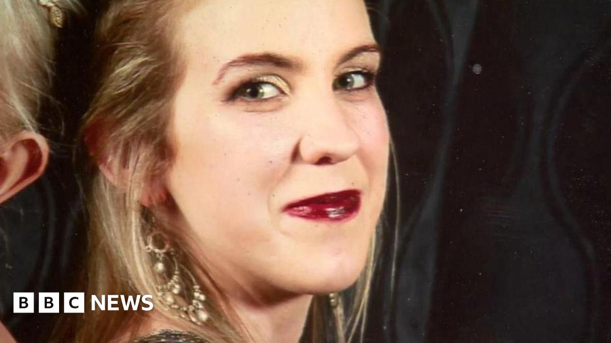 A smiling Natalie McNally. She has blonde hair and is wearing earrings and red lipstick