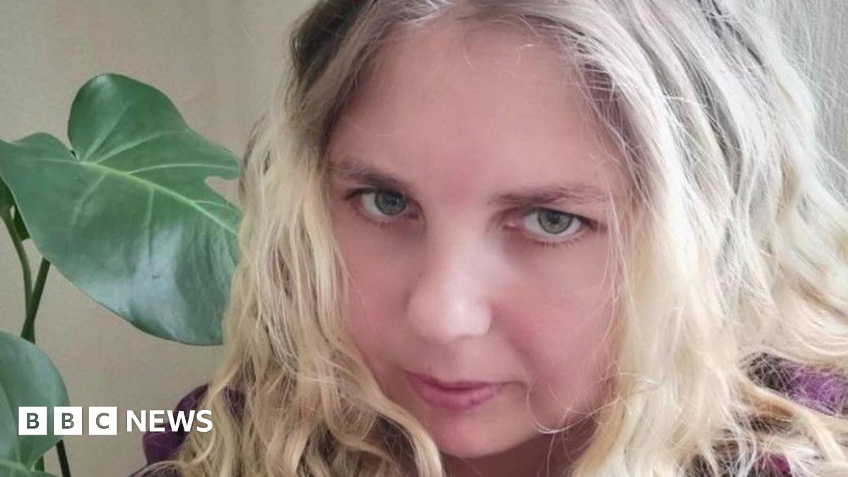 Alexia Nazarova, a woman with blonde hair, looking into the camera. She is wearing a purple jumper and there is a green plant beside her.