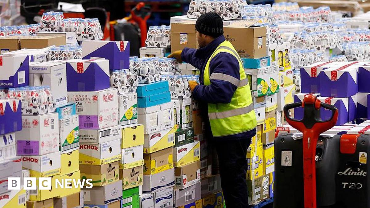 A worker wearing a hi-vis jacket stacks shelves in a supermarket warehouse.
