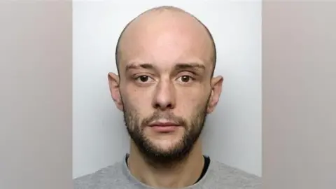 West Yorkshire Police A police mugshot of Calum Sunderland. He is bald with a brown beard. He is wearing a grey jumper.