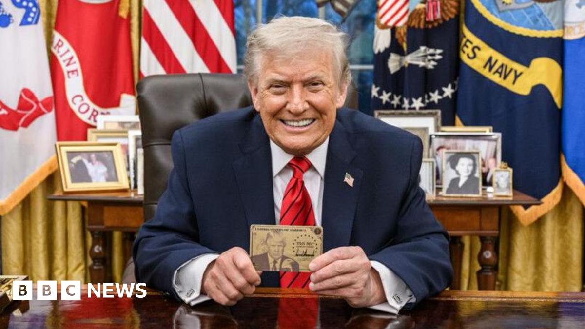 President Donald Trump smiles for the camera in the White House and he holds up a Trump Gold Card