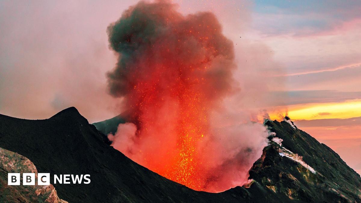 Eight people dressed in white robes and pointed hats walk in bare feet in a procession behind a group of three men in colourful clothes. The men carry flags.