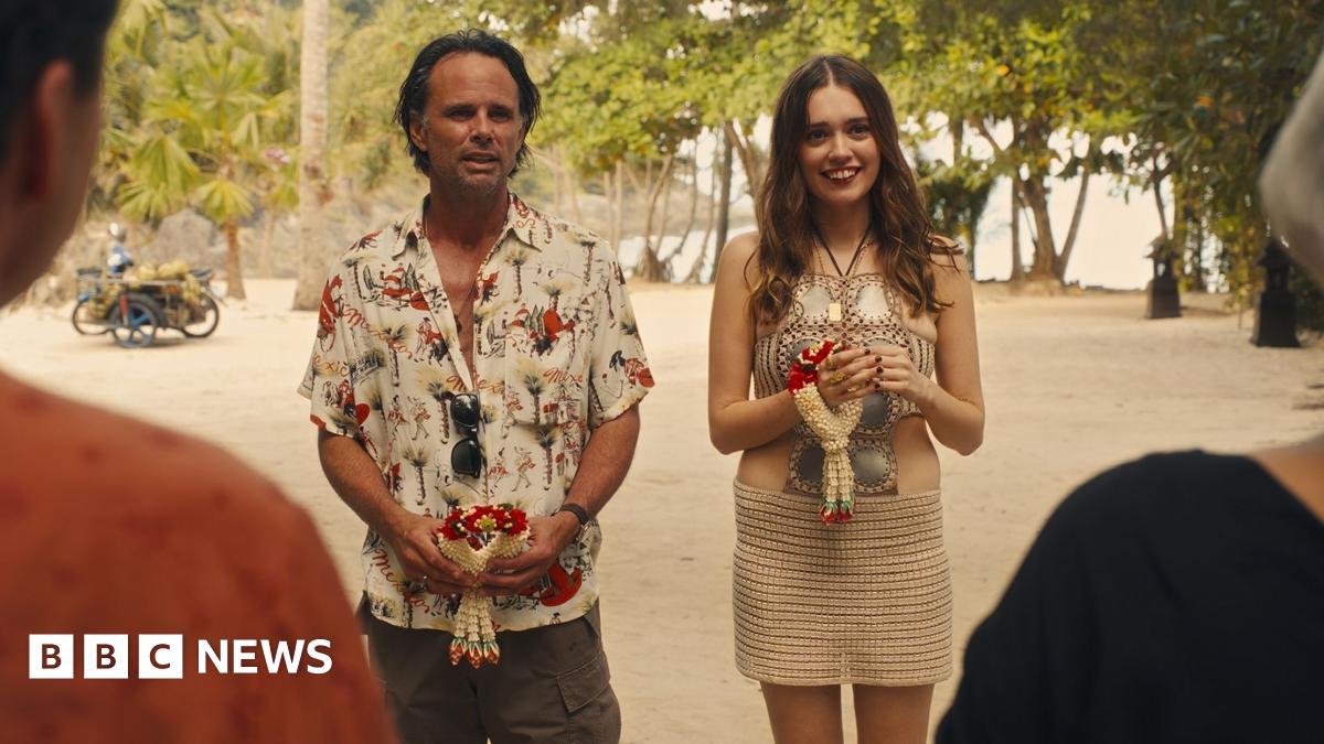 Walton Goggins and Aimee Lou Wood,  in costume, stand next to each other on a beach in a scene from the White Lotus