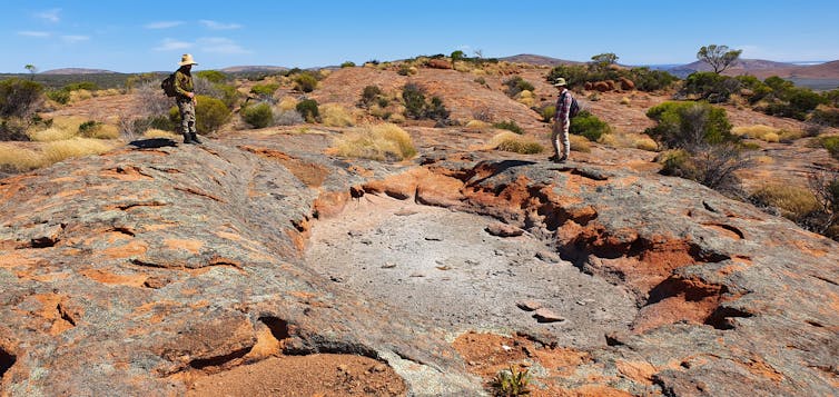 A dry rock-hole in a large granite outcrop. Two field workers stand nearby.