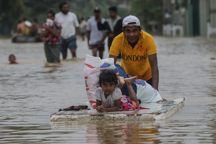 man pushing floating door with daughter on it through floodwaters.