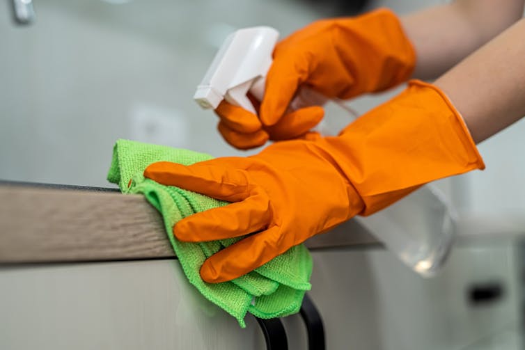 Person wearing rubber gloves, spraying a kitchen-counter top with antibacterial spray.