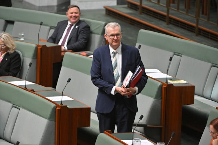 A man in a suit holding some papers in the Australian House of Represenatives.