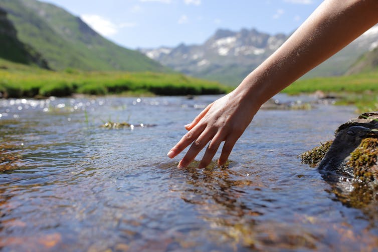 Person trails hand in stream with hills in the background.