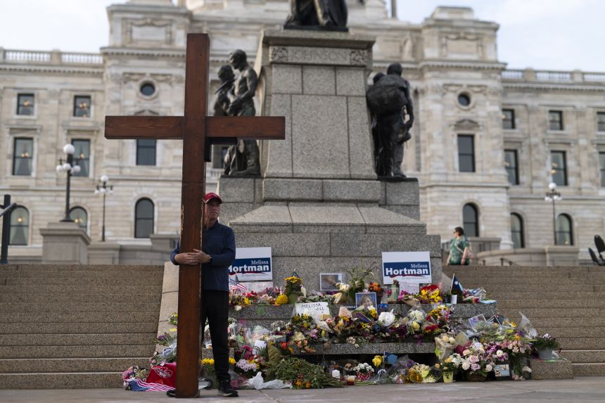 Beazley holds the cross next to a memorial for Minnesota state Rep. Melissa Hortman and her husband, Mark, outside the Capitol building in St. Paul on June 18, 2025. The Hortmans were shot and killed at their home in what the governor called a 
