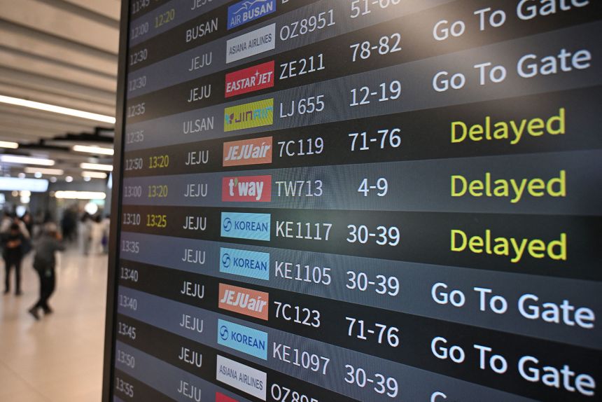 Passengers walk past an information board showing delayed flights at Gimpo airport in Seoul on November 13, on the day of the annual college entrance exam.