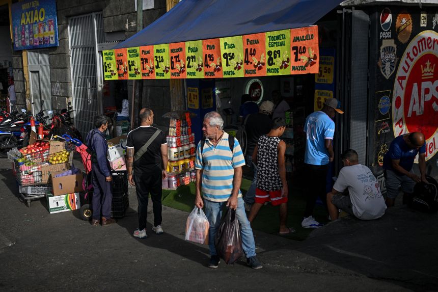 A man holds a grocery bag in front of a store displaying signs with dollar prices at the Quinta Crespo municipal market in Caracas on November 13.