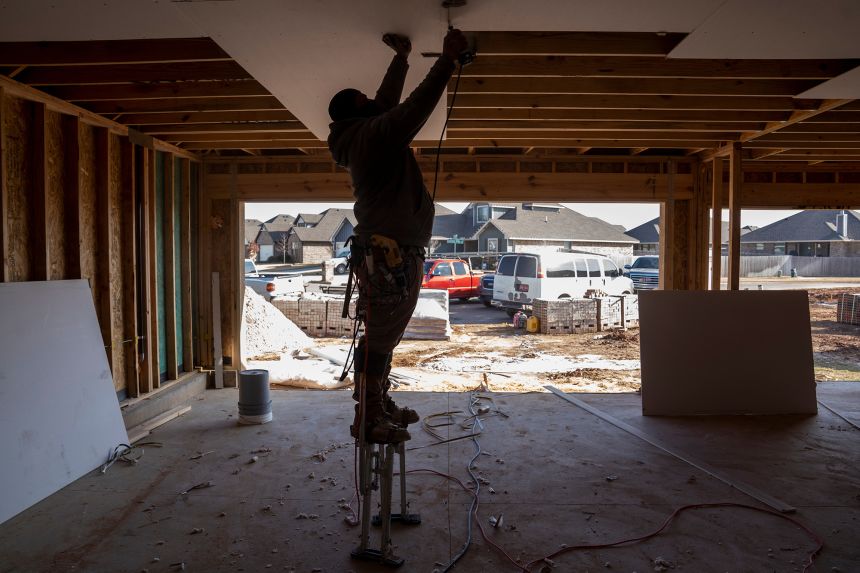 A worker hangs drywall for a new home under construction at a development in Yukon, Oklahoma, on December 5, 2025.