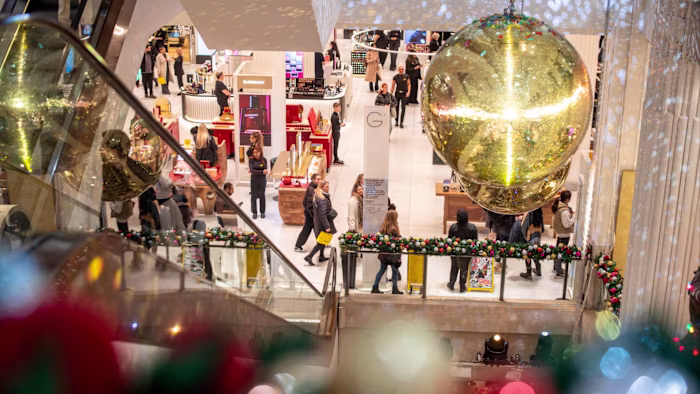 Shoppers walk through Selfridges decorated with large gold ornaments and festive garlands for Christmas.