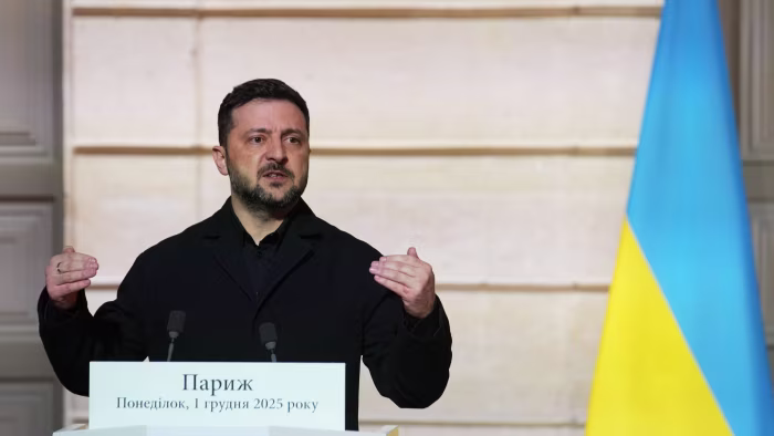 Volodymyr Zelenskyy delivers a speech at a podium with a Ukrainian flag visible in the background.